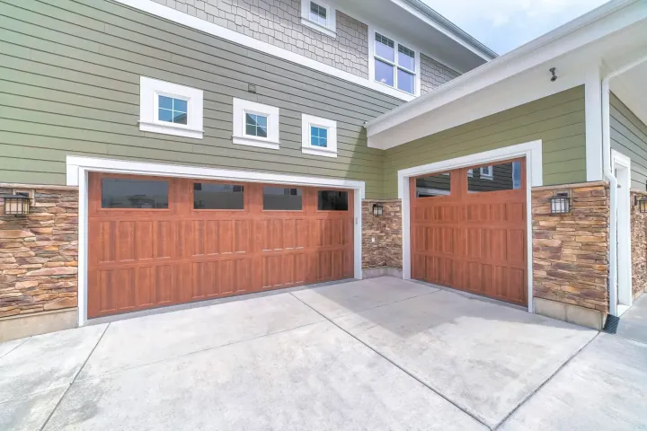 Two-story home exterior with wood-tone garage doors and stone accents