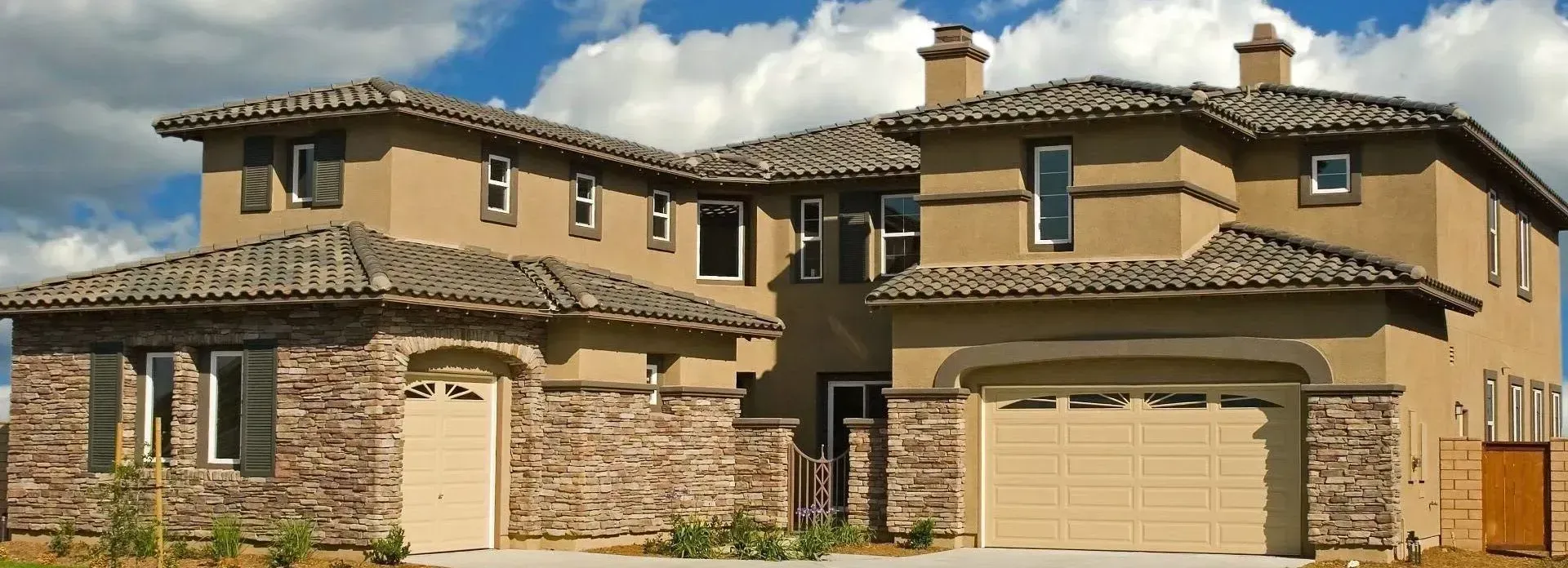 Two-story stucco home with a tile roof and stone-trimmed white garage door
