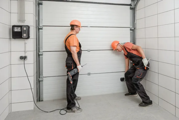 Two technicians drilling and securing a garage door panel section during installation in Scottsdale, AZ