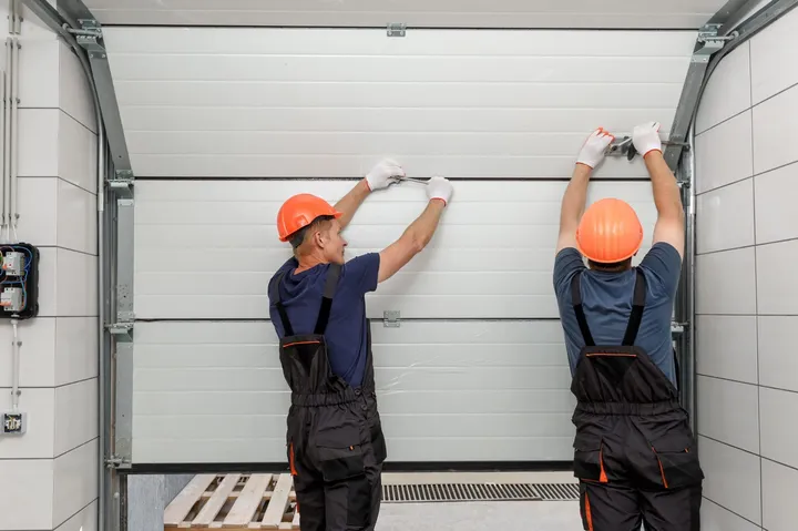 Two technicians installing an overhead sectional garage door panel in Paradise Valley, AZ