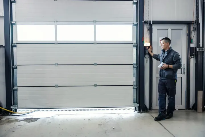 Technician checking door balance beside a tall white sectional garage door on a Sun City, AZ spring service call