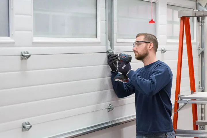 Technician driving a bracket bolt on a windowed sectional door during a Peoria, AZ garage door spring repair