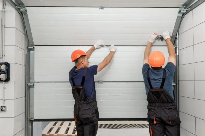 Two technicians tightening hinge hardware on a white sectional door during a Glendale, AZ spring replacement