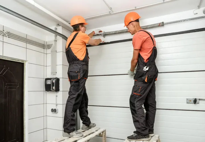 Two technicians installing a garage door torsion spring and track inside a residential garage
