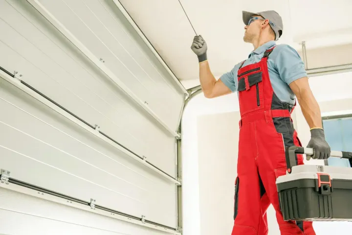 Technician carrying a toolbox to inspect an overhead garage door track